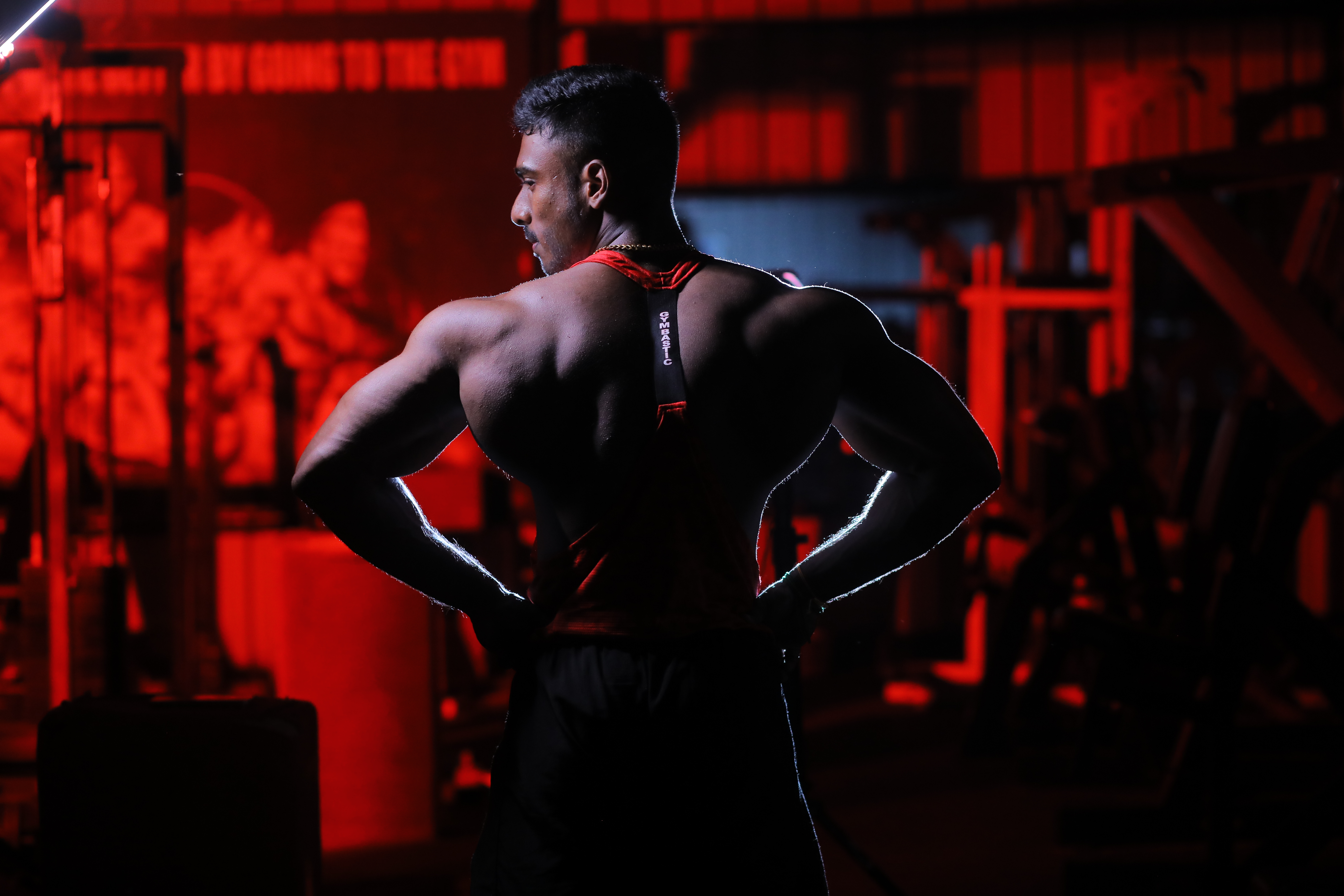Coach Mohan back pose in red-lit gym
